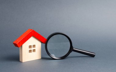 Ahşap ev ve gri bir arka plan üzerinde büyüteç. Gayrimenkul satın alma ve satma, yeni binalar, ofisler ve evler inşa. Ev araması. Kentsel planlama kavramı, altyapı projeleri