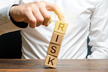 İşadamı, düşen Risk yönetimi, maliyet değerlendirmesi, iş ve yatırım güvenliğinden kaynaklanan risk kelimesi ile bir küp kulesini parmağıyla kurtarır. İş esnekliğini ve esnekliğini güçlendirmek.