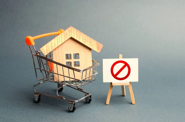House in the shopping cart and the sign of the ban NO. Inaccessible and expensive housing. Seizure and freezing of assets by a bank, court. Unavailability of housing, busy or low supply — Stock Photo, Image
