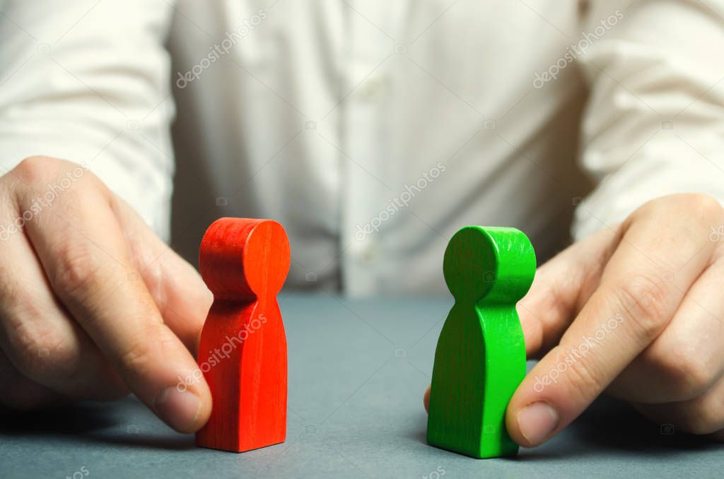 A man holds in his hands the red and green figures of people facing each other. Conflict resolution, conflict of interest. The search for a compromise, mediation in negotiations. Weave intrigue.