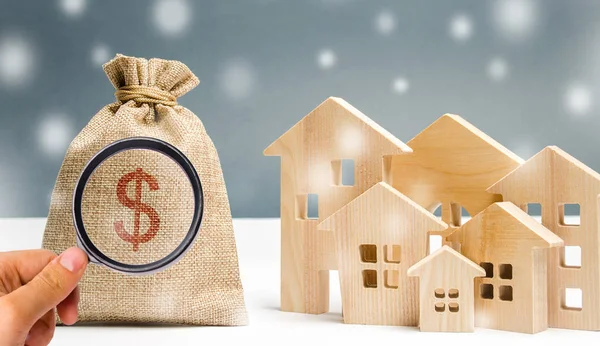 Money bag and a wooden houses with snow. Conceptual image real estate market in the winter season. Christmas sale / discounts concept. Housing demand. Mortgage, loan, credit. Budget — ストック写真