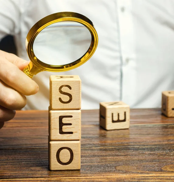 Blocks with the word SEO and a magnifying glass in the hand of a businessman. Search Engine Optimization. Increase the quality and quantity of website traffic by increasing the visibility of a website