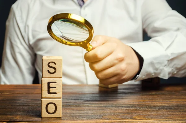 Blocks with the word SEO and a magnifying glass in the hand of a businessman. Search Engine Optimization. Increase the quality and quantity of website traffic by increasing the visibility of a website