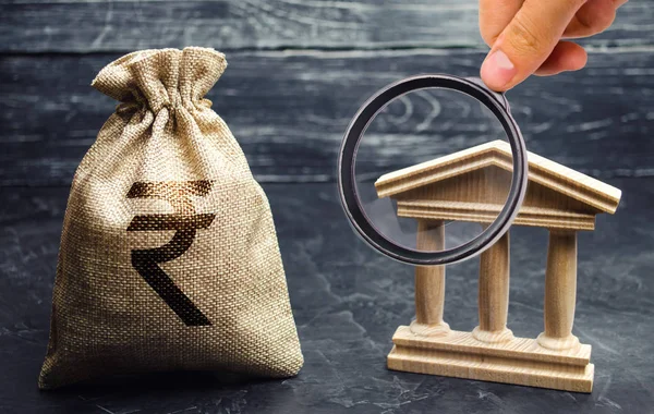 stock image A bag with indian rupee (rupiah) and a government building. Money turnover. Deposits, investment and loan. Grants and subsidies. Payment of taxes. Credit tranches and leases. Debt repayment. Bank.