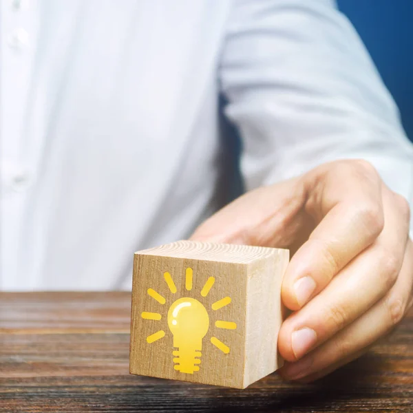 Businessman holds a wooden block with an image of a light bulb idea. Generation of innovative business ideas. Creative process. The accumulation of experience and skills.