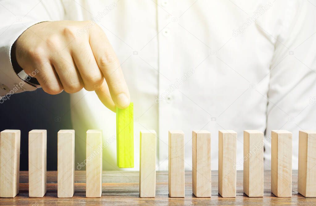 A man puts green dominoes in a row. Business management and processes. Correct errors, make improvements. Risk management, integration into upgrades to the system, implementation into legislation.