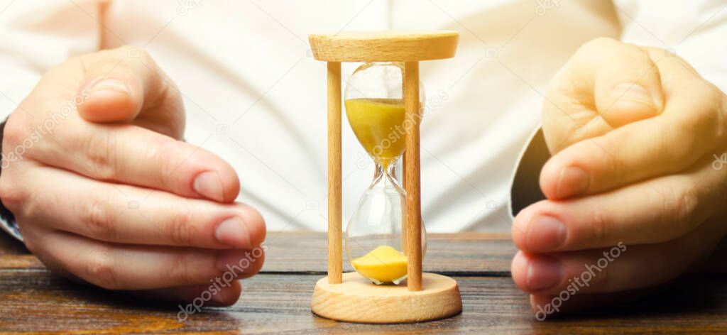 Man protects the hourglass. Concept of saving time and money. Time management. Planning work. Reduced cost and bureaucratic burden. Saving productivity. Extension of life. Debt / tax holidays