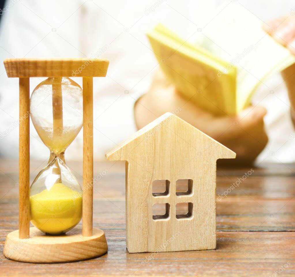 Wooden house and clock. Businessman counting money. Payment of deposit or advance payment for renting a home or apartment. Long-term mortgage on the house. Tax and mortgage vacations. Pledge