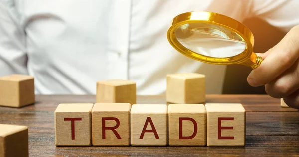 Businessman holds a magnifying glass over the word Trade. Business market and finance concept. Transfer of goods or services. Money, economy. Business deal. Trading on the stock exchange