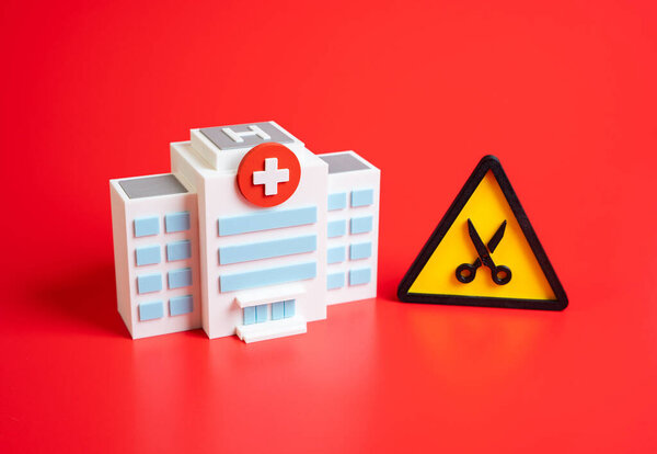 Hospital and the symbol of cuts. Cost reduction or dismissal of staff. Symbol of healthcare crisis, budget shortages, staff layoffs, medical closures, and public health decline.