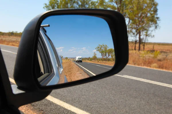 View in the side mirror on the Carnarvon Highway in Central Queensland Australia. 4WD vehicle towing caravan and outback Australian landscape