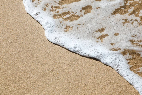 Onda angulada com espuma sobre areia — Fotografia de Stock