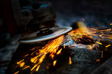 İşçi metal bir yüzeyi öğütücüyle parlatıyor. Metal testereyle kesiliyor..