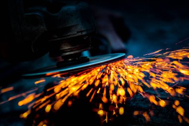 İşçi metal bir yüzeyi öğütücüyle parlatıyor. Metal testereyle kesiliyor..