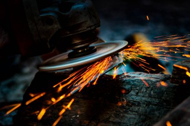 İşçi metal bir yüzeyi öğütücüyle parlatıyor. Metal testereyle kesiliyor..