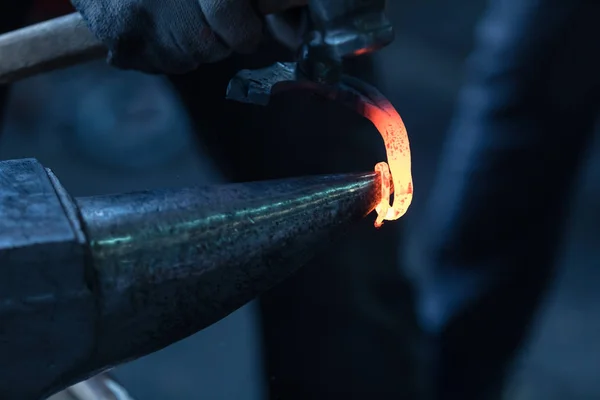 The smith behind work. In hands at the smith nippers which he holds the warmed piece of metal. Leaning on an anvil the smith forges a metal figured detail. Metal red from temperature