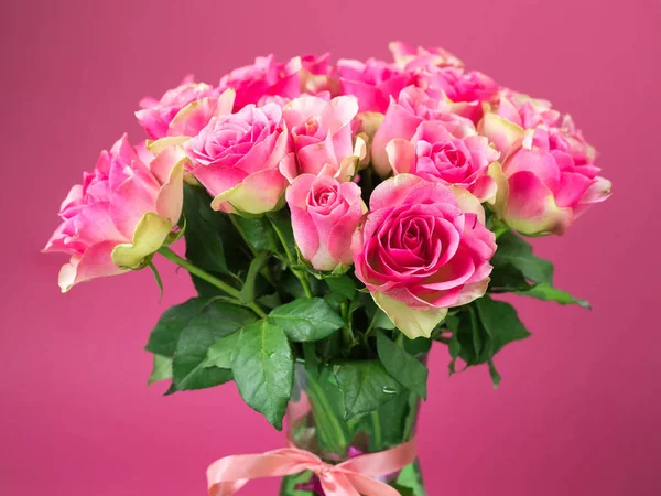 Bouquet of pink roses in a glass vase on a pink background.