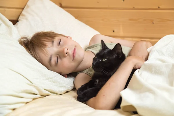 Caucasian boy 8 years old sleeps in bed hugging his beloved pet black cat