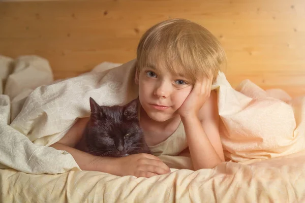 Kaukasische jongen 8 jaar oud wakker in de ochtend in bed knuffelen huisdier zwarte kat — Stockfoto