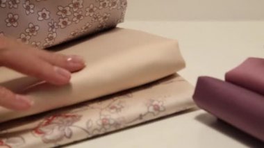 Kadınların elleri ütüleme ve pembe ve bej çiçek pamuklu kumaşlar ile kesim dokunmadan. Kumaşlı bir yığın üzerinde ton iplikleri ile büyük bir bobin var
