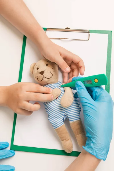 Médico e a criança segurar o termômetro e medir a temperatura do urso de brinquedo . — Fotografia de Stock