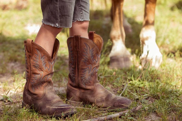 The childs legs in cowboy boots and the legs of the horse next to each other. Cowboy concept. — Stock Photo, Image