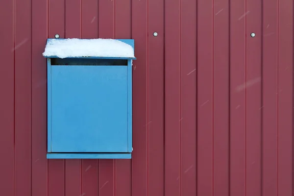 Blue mailbox hangs on a burgundy fence