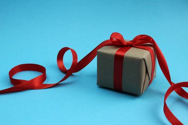 Mavi bir arka plan üzerinde kırmızı fiyonklu bir hediye ile gri kutu