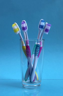 Beş diş fırçası mavi bir arka plan üzerinde bir cam kabın içinde duruyor