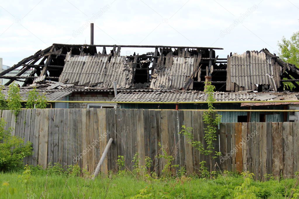Dilapidated rural house after the fire stands behind the fence