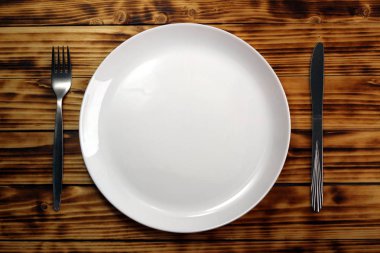 Plaka, çatal ve bıçak ile masa ayarı. Koyu ahşap arka planda beyaz boş plaka, gümüş çatal ve bıçak.