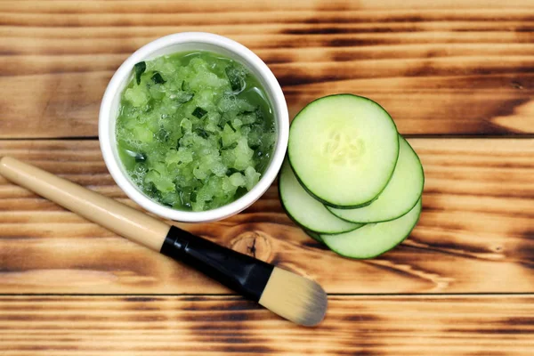 Bir salatalık maskesi ve masanın üzerinde bir fırça ve arka planda salatalık ile Bowl