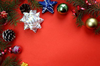 Kırmızı arka planda Noel deseni köknar dalları, oyuncaklar ve koniler