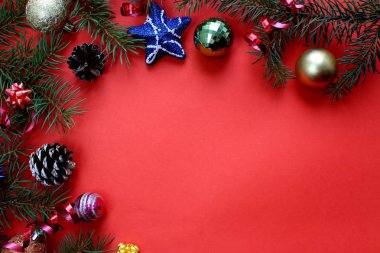 Kırmızı arka planda Noel deseni köknar dalları, oyuncaklar ve koniler