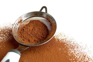 Beyaz arka planda süzgeci olan kakao tozu