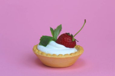 Kremalı tart ve pembe arka planda olgun çilek.