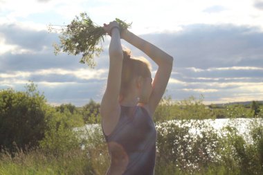 Açık havada bir buket kır çiçeğiyle bir kız ellerini kaldırıyor.