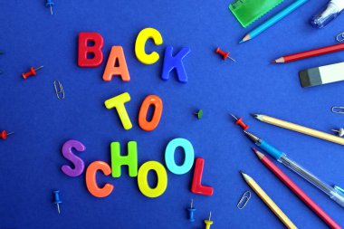 Kırtasiye malzemeleriyle çevrili mavi yüzey üzerinde okula dönüş mektubu