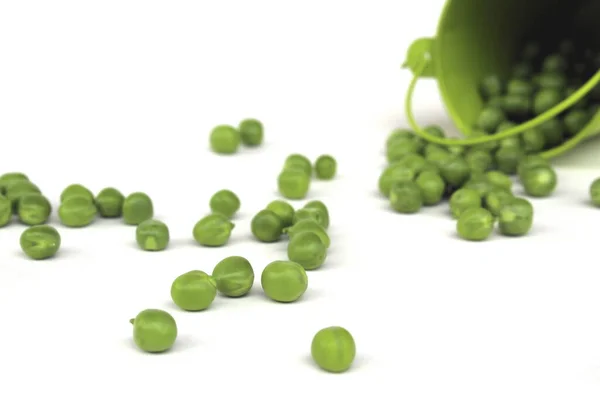 白い表面に散在緑のエンドウ豆と緑のバケツを覆した — ストック写真