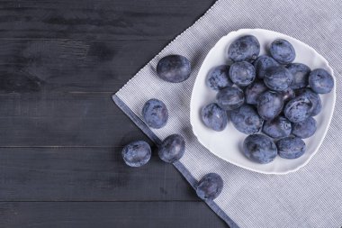 Koyu ahşap bir masa üzerinde beyaz bir tabakta taze erik bir sürü 
