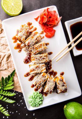 Japon yılan balığı ile kireç, soya sosu ve yemek çubukları ile siyah bir zemin üzerine rulo