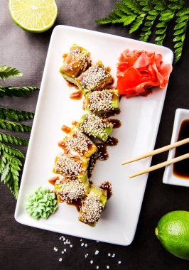 Japonca kireç, soya sosu ve yemek çubukları ile siyah bir zemin üzerine avokado, yılan balığı ve omlet ile rulo