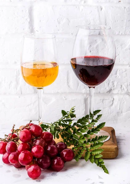two glasses of white and red wine with a bunch of grapes on a white concrete background