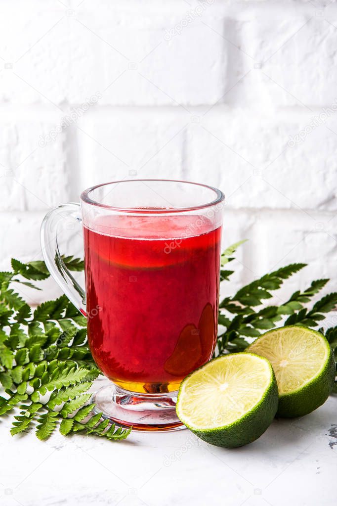 berry tea with lime in a glass cup on a white wall background