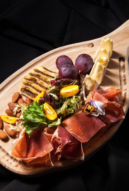 Salam, jambon, bree peynir, üzüm ve badem fındık karanlık şık arka plan üzerinde bir kesme tahtası üzerinde et Şarküteri