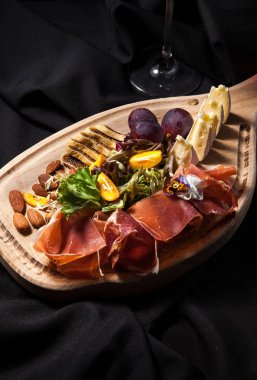 Salam, jambon, bree peynir, üzüm ve badem fındık karanlık şık arka plan üzerinde bir kesme tahtası üzerinde et Şarküteri
