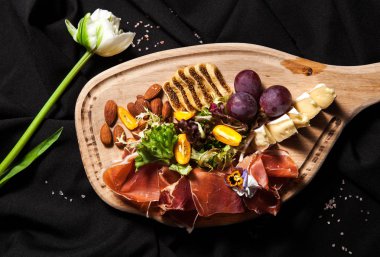 Salam, jambon, bree peynir, üzüm, badem fındık, karanlık bir şık arka plan üzerinde Beyaz Lale ile kesme tahtası üzerinde et Şarküteri