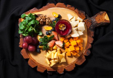 Bir kesme tahtası ile fındık, üzüm ve şarap koyu şık arka plan yakın çekim üzerinde peynir türleri ayarlama