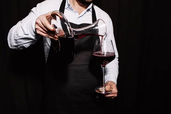 侍酒师正在黑暗的背景下将红酒倒进酒杯里 — 图库照片