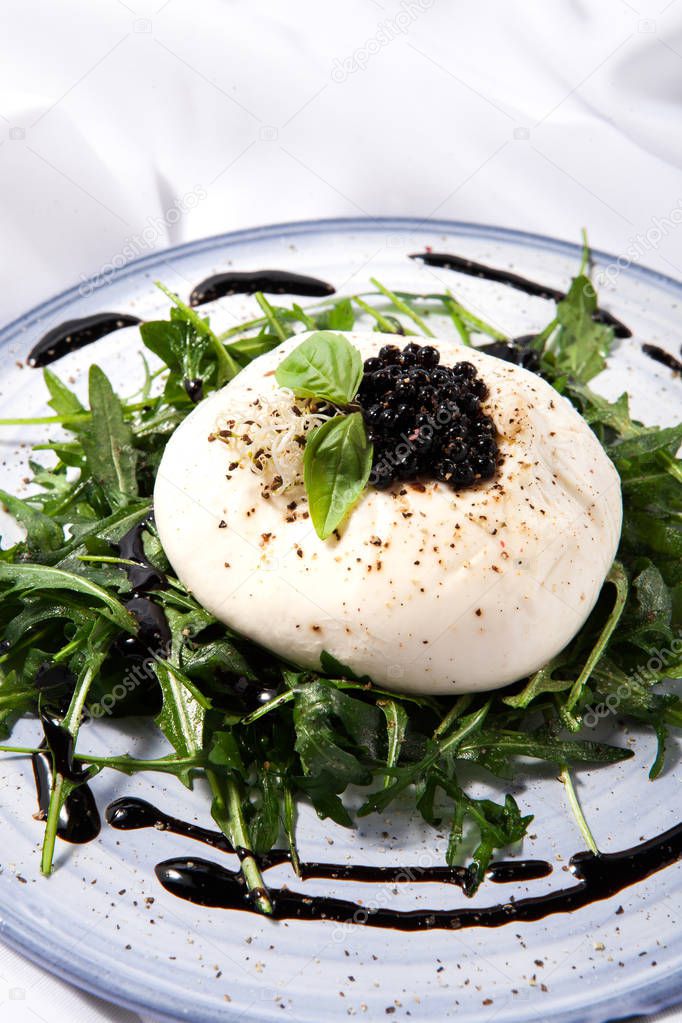 Burratta cheese with arugula and balsamic vinegar pearls on a white background